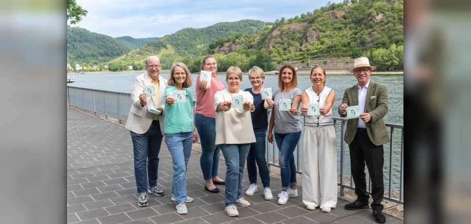 Bürgermeister Jörg Haseneier (rechts), die Vorsitzenden der Werbegemeinschaft Boppard, Nicole Weißer (2. von rechts), der Leiter der Tourist Information Boppard, Michael Defrancesco (links), und das Team der Tourist Information präsentieren das neue Bopparder Sticker-Motiv: „Boppard freut sich auf die BUGA29“. 