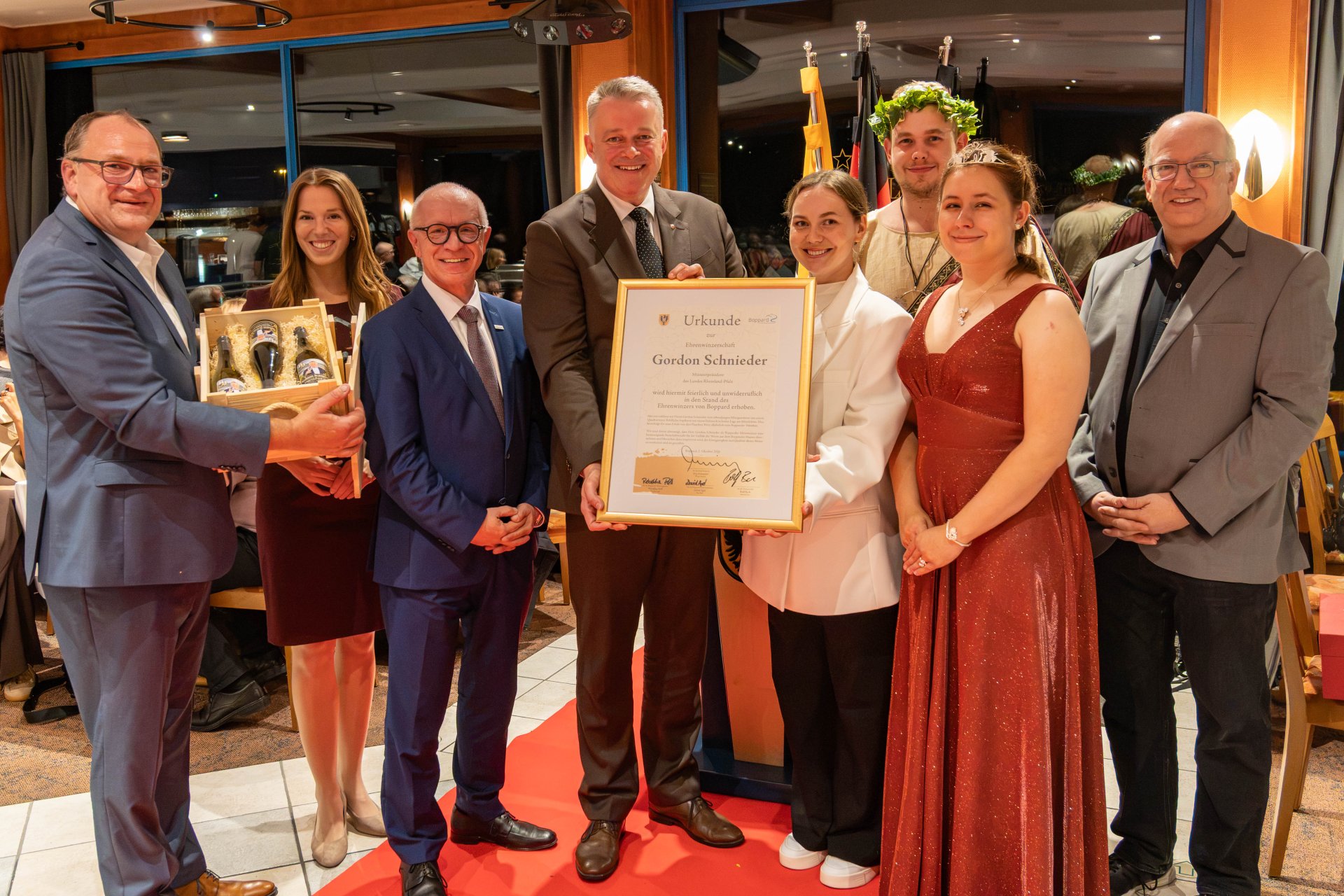 Höhepunkt des Abends war die Verleihung der Bopparder Ehrenwinzerwürde an Ministerpräsident Gordon Schnieder (4. von links). Boppards Bürgermeister Jörg Haseneier (3. von links) überreichte die Auszeichnung gemeinsam mit (von links) Patenwinzer Rolf Bach, Moderatorin und ehemalige Deutsche Weinprinzessin Julia Lambrich, Yuliia Babak, Mitarbeiterin der Tourist Information Boppard, Bacchus David Apel, Boppards Weinkönigin Rebekka Perll und Michael Defrancesco, Leiter der Tourist Information Boppard. 