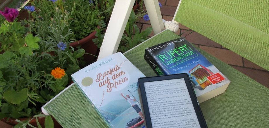 Das Foto zeigt Bücher und einen E-Book-Reader auf einem Gartenstuhl.