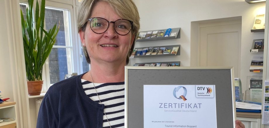 Das Foto zeigt die Mitarbeiterin der Tourist Information Boppard, Claudia Rheinbay, die ein Zertifikat des Deutschen Tourismusverbands in ihren Händen hält.