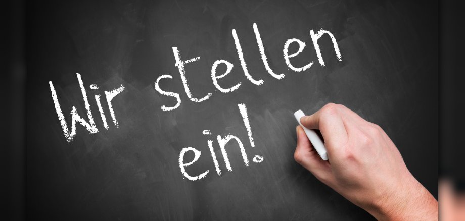 hand writing 'We are hiring!' in German on a chalkboard