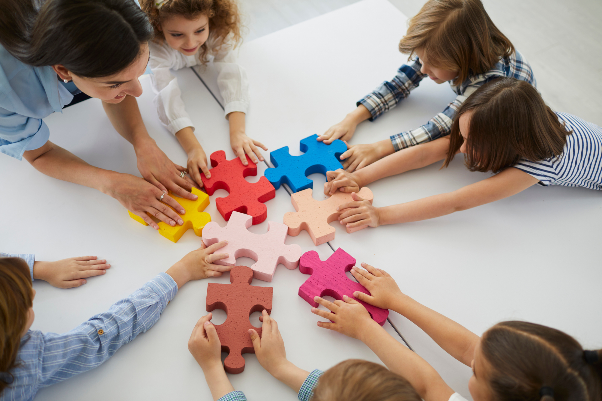Team of creative little children with teacher put together pieces of jigsaw puzzle