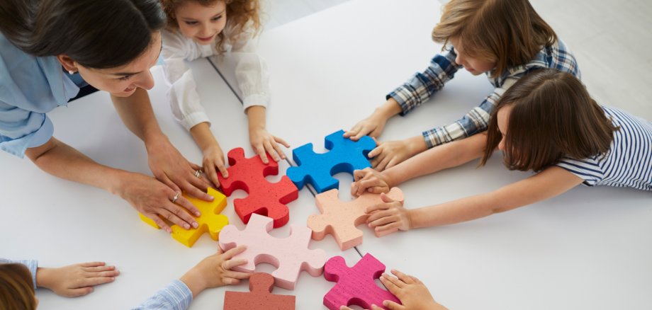 Team of creative little children with teacher put together pieces of jigsaw puzzle
