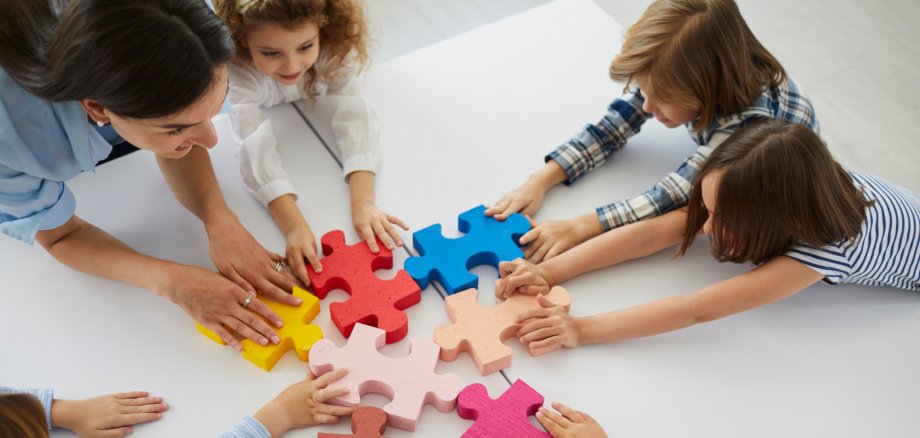 Team of creative little children with teacher put together pieces of jigsaw puzzle
