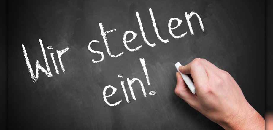 hand writing 'We are hiring!' in German on a chalkboard