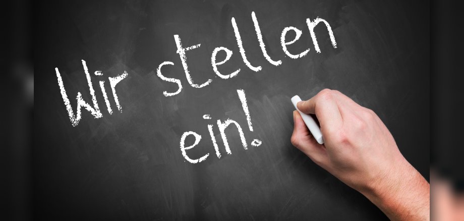 hand writing 'We are hiring!' in German on a chalkboard