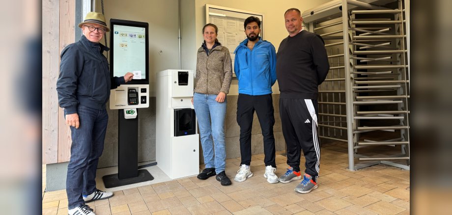 Bürgermeister Jörg Haseneier (von links) und Ortsvorsteherin Alexa Bach testeten den neuen Kassenautomaten im Thermalfreibad in Buchenau und erstanden die ersten Freibadtickets für die Saison 2026. Mit ihnen freuen sich Rettungsschwimmer Bsher Almanfi und Betriebsleiter Christian Meinecke auf zahlreiche Badegäste. 